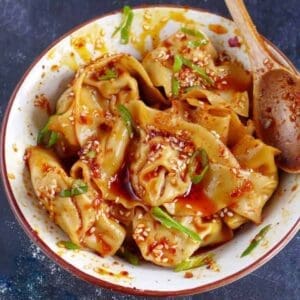 Bowl of spicy dumplings in chili oil with scallions
