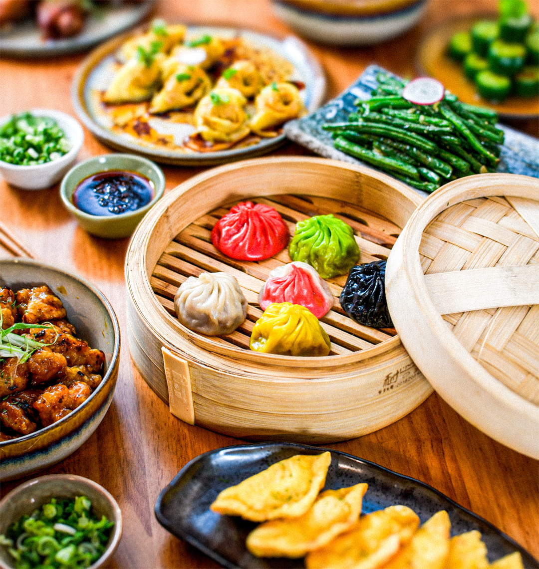 Table full of food at Ugly Dumpling, Including XLB, wontns, green beans, cucumber salad and wings. 